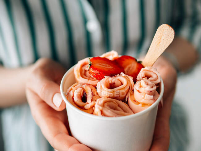 Rolled ice cream with strawberry in cone cup in woman hands. Hand holding cone cup with thai style rolled ice cream — Stock Photo
