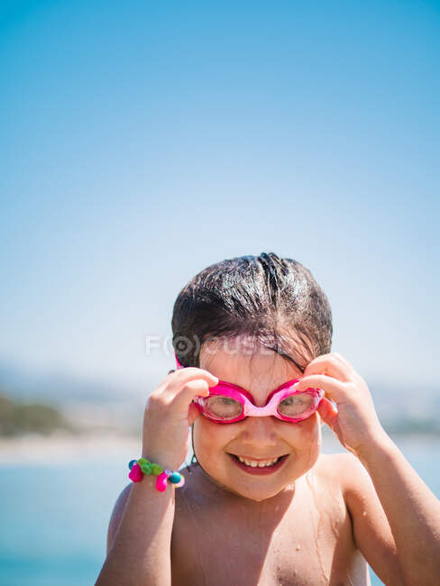 Cute smiling female kid taking off goggles after swimming in sea on background of blue sky — Stock Photo