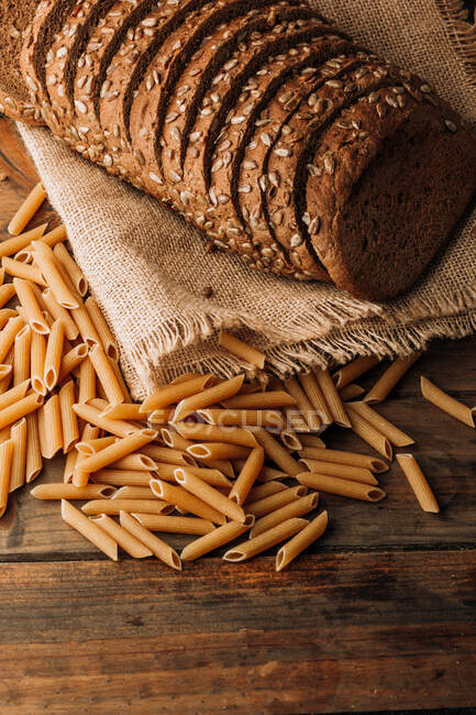 D'en haut pâtes et pain de seigle parfumé fraîchement soutenu avec des graines sur serviette de lin sur fond en bois — Photo de stock