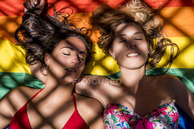 Pareja lesbiana acostada en la bandera del arco iris - foto de stock