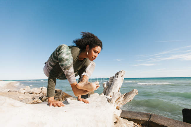 Афроамериканская привлекательная молодая женщина, занимающаяся титибасаной йогой на пляже — стоковое фото
