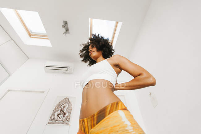 Africano americano atraente jovem mulher realizando postura de ioga com as mãos atrás das costas na sala de luz — Fotografia de Stock