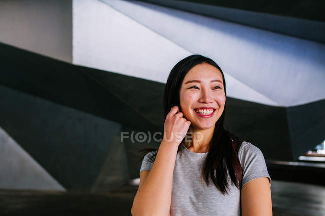 Emocionado mujer asiática en traje casual alegremente sonriendo mientras mira hacia otro lado - foto de stock