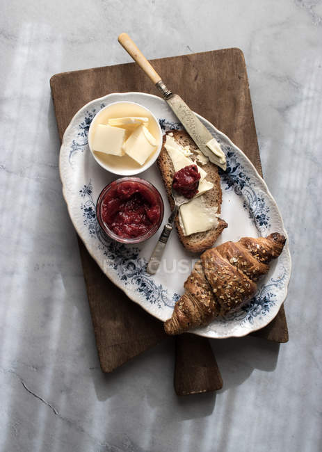 Croissant croustillant et pain grillé au beurre et confiture de fraises servi sur planche de bois — Photo de stock