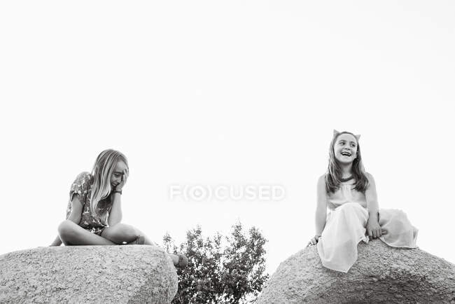 Von unten lachende kleine Mädchen in Kleidern, die auf Felsbrocken in der Natur sitzen — Stockfoto
