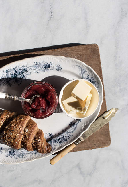 Piatto di croissant croccante e burro e marmellata di fragole servito su tavola di legno — Foto stock