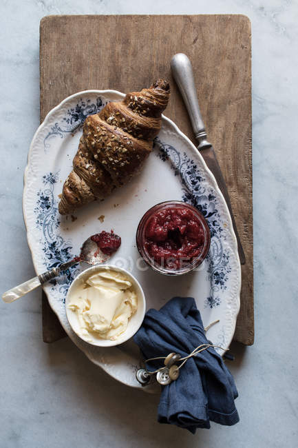 Knusprige Croissants mit Butter und Erdbeermarmelade auf Teller auf Holzbrett serviert — Stockfoto