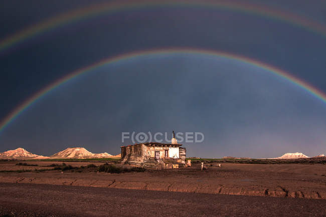 Lonely old house in desert and rainbow in stormy sky — Stock Photo