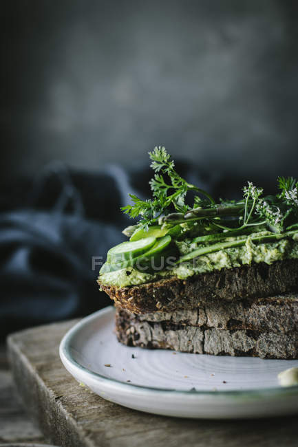 Toasts mit grüner Cashewpastete, Kräutern und Gurkenscheiben auf Holzbrett — Stockfoto