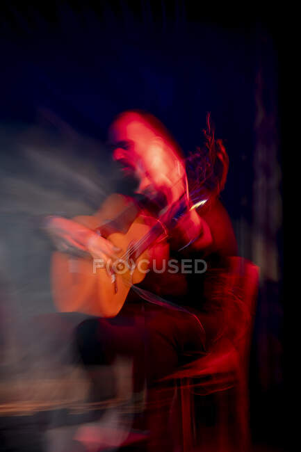 Hispanic man playing acoustic guitar during flamenco performance on dark stage — Stock Photo