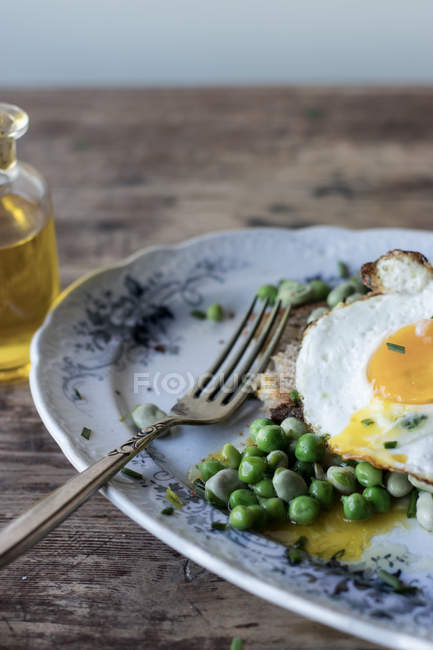 Closeup of served plate with sauteed green peas and fried egg on wooden table — Stock Photo