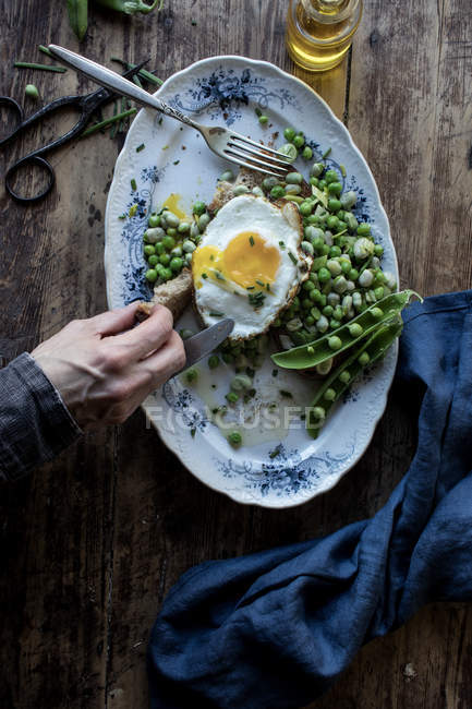Mão humana degustação de prato servido com ervilhas verdes refogados e ovo frito na mesa de madeira — Fotografia de Stock