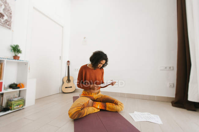 Afroamericana atractiva joven sentada con las piernas cruzadas y comprobando papeles de rutina - foto de stock