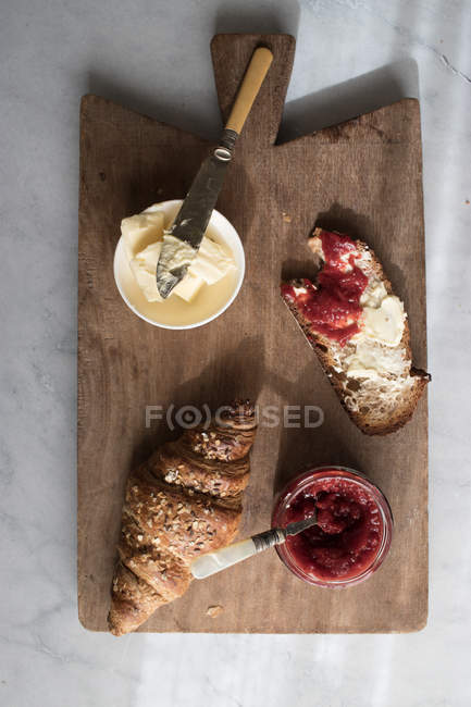 Knusprige Croissants mit Butter und Erdbeermarmelade auf Holzbrett serviert — Stockfoto