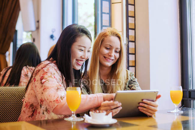 Молода кавказька жінка насупилася і показувала відеофільм на планшеті до здивованого азіатського друга, сидячи за столом у кафе. — стокове фото