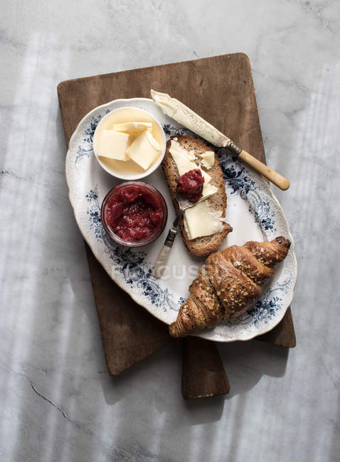 Croissant croccante e pane tostato con burro e marmellata di fragole serviti su tavola di legno — Foto stock