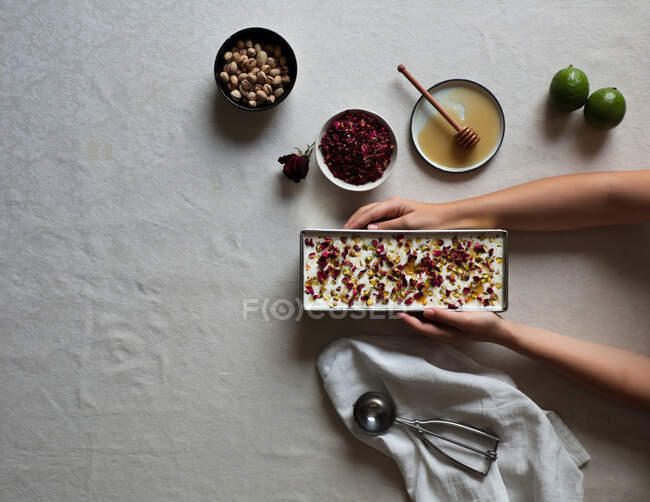 Mains de femelle anonyme mettant récipient avec délicieux gâteau au fromage sur la table près de limes et miel avec des épices — Photo de stock