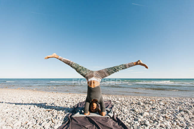 Афроамериканская молодая женщина в стойке на голове на фоне спокойного моря в солнечный день — стоковое фото