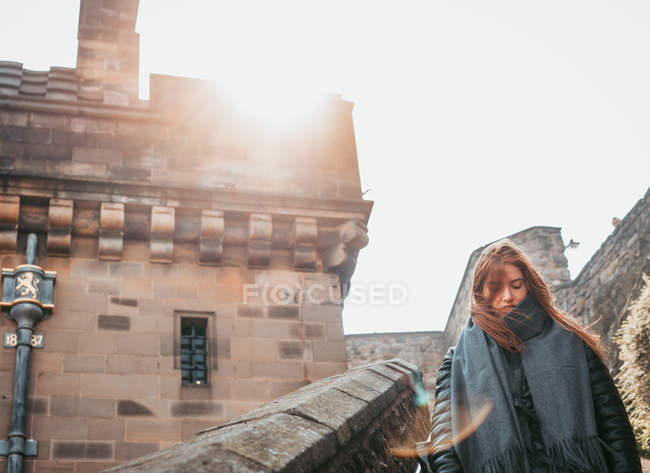 Trendy woman in black outfit walking on paved old street with stone building, Scotland — Stock Photo