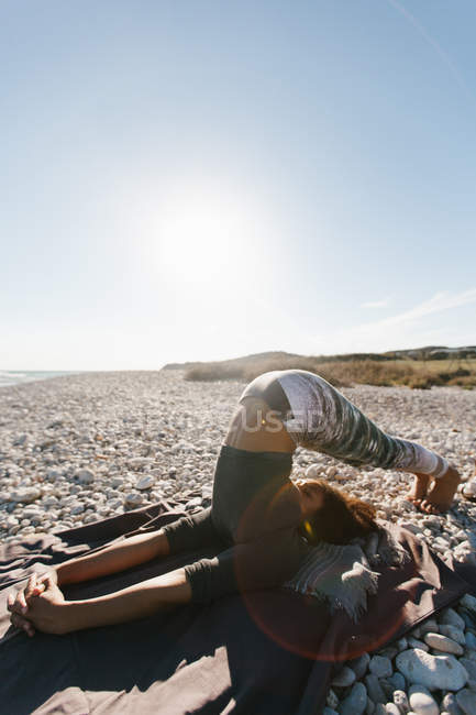 African American young woman in yoga headstand posture on background of calm sea in sunny day — Stock Photo