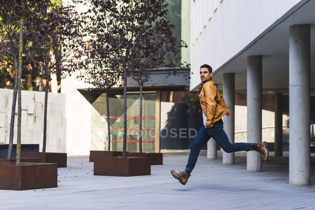Trendy man in casual outfit looking at camera while running outside modern building — Stock Photo