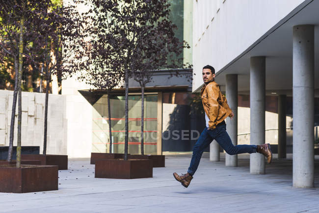 Uomo alla moda in abito casual guardando la fotocamera mentre corre fuori edificio moderno — Foto stock