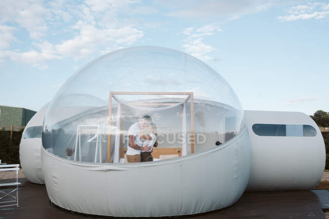 Side view of passionate man and young woman while standing inside of romantic transparent glamping — Stock Photo