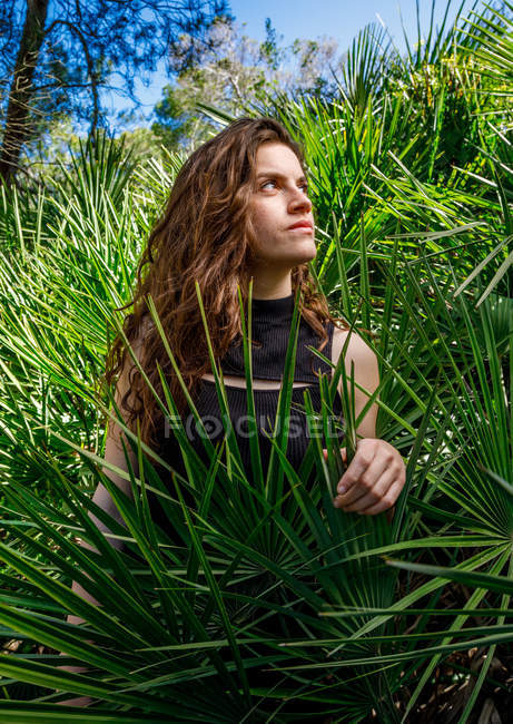 Брюнетка женщина стоит в тропических кустах и смотрит в сторону — стоковое фото