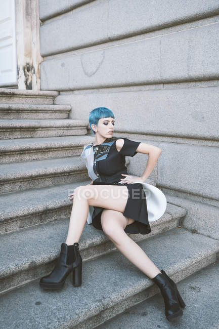 Young woman with short blue hair wearing trendy informal dress and posing on street steps — Stock Photo