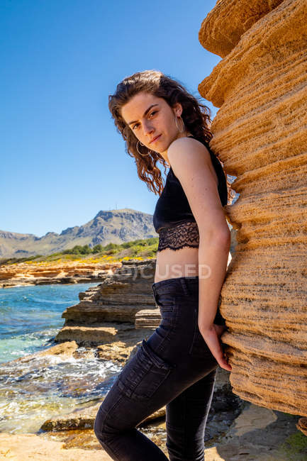 Slim young woman in black crop top and jeans standing in canyon and looking at camera — Stock Photo