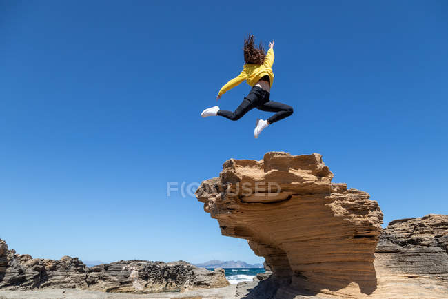 Expressive woman making extreme trick above big rocky stone in wild desert area on background of blue sky — Stock Photo