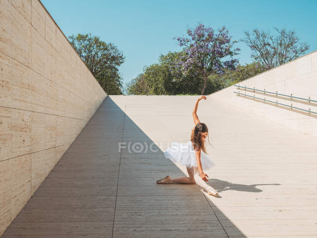 Балерина выступает с поднятыми руками и вытянутыми ногами на улице в яркий солнечный день — стоковое фото
