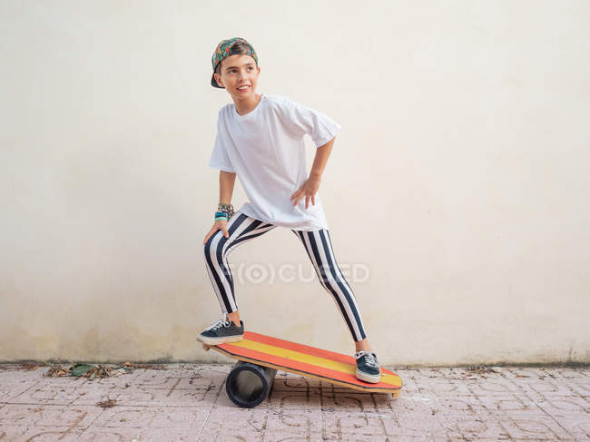 Стильный симпатичный мальчик в трико, выполняющий трюк на яркой доске и смотрящий в камеру на белом фоне — стоковое фото