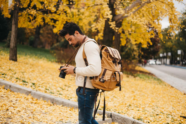 Handsome young photographer standing in autumn park and holding camera — Stock Photo