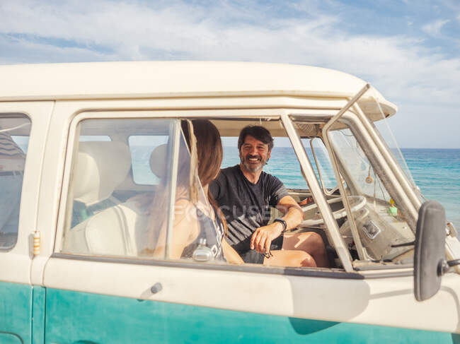 Бородатый мужчина и длинноволосая женщина в красочных солнцезащитных очках сидят перед морем машины и смотрят на голубую игрушечную машинку — стоковое фото