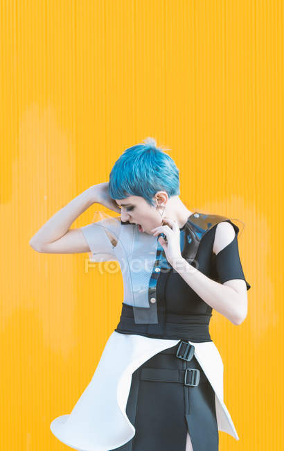Sensual young woman in trendy futuristic dress screaming while standing on pavement against bright yellow wall — Stock Photo
