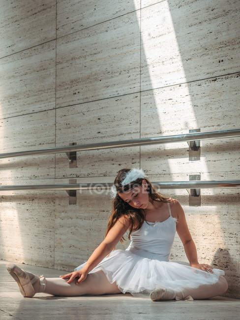 Bailarina sentada en el suelo estirando elegante pierna en el aula - foto de stock