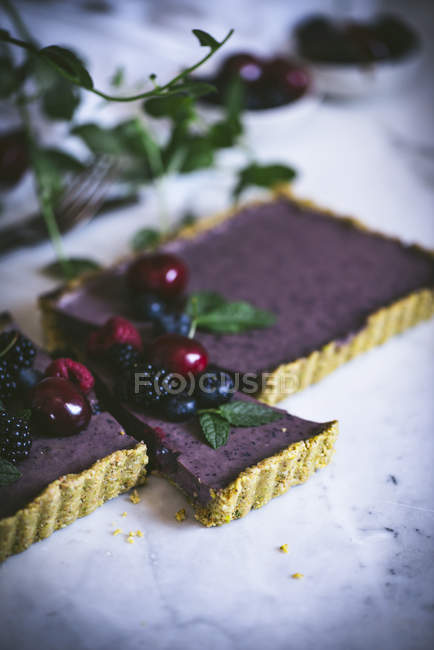 Sliced tasty rectangular cake decorated with summer berries on white table — Stock Photo