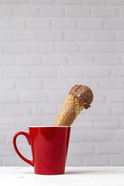 Cono de helado de chocolate en taza roja contra la pared de ladrillo blanco - foto de stock
