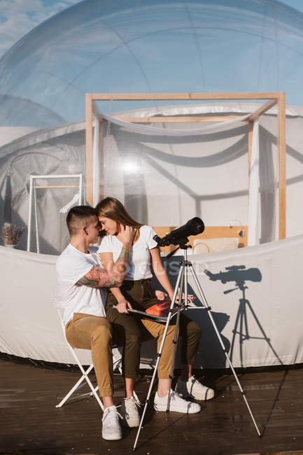 Elegante donna seduta in grembo fidanzato dal telescopio vicino bolla hotel — Foto stock