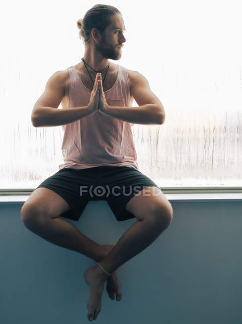 Расслабленный вдумчивый мужчина, сидящий в гармонии рядом с парящим окном и отворачивающийся — стоковое фото