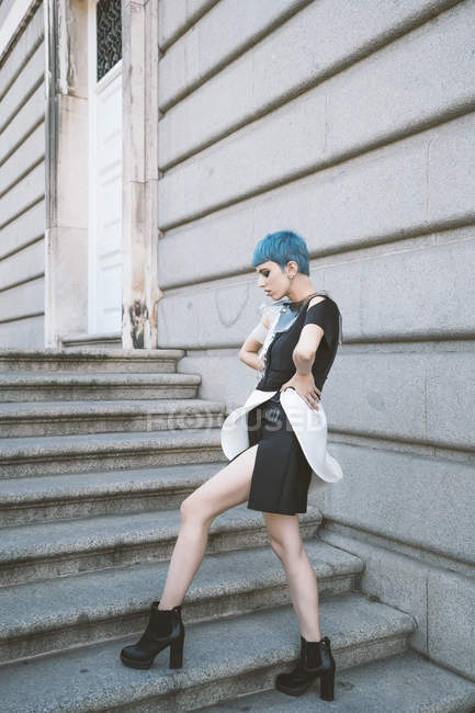 Junge Frau mit kurzen blauen Haaren trägt trendiges informelles Kleid und posiert provokant auf den Stufen der Straße — Stockfoto