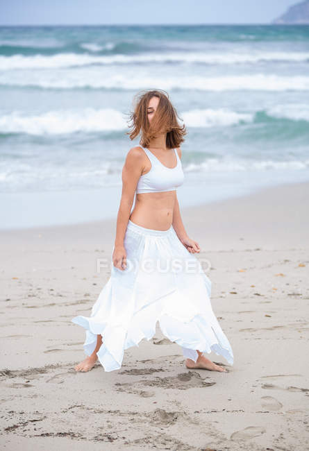 Приваблива жінка в білому вбранні танцює на піску біля махаючого моря — стокове фото