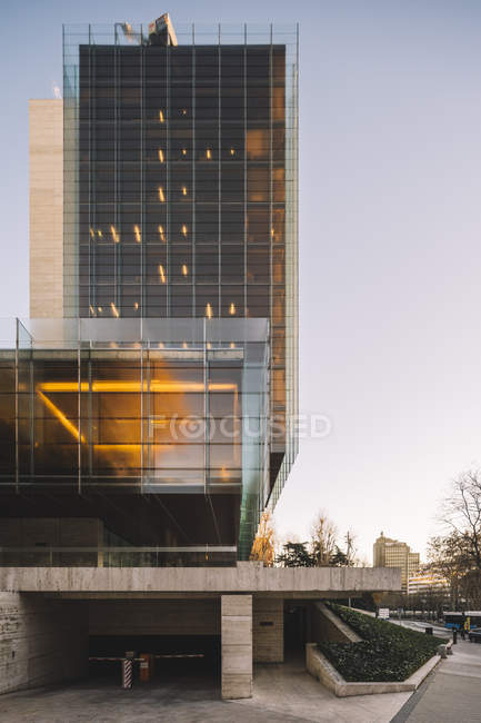 Arranha-céu de vidro elegante com estacionamento refletindo sol em dia brilhante no centro da cidade — Fotografia de Stock
