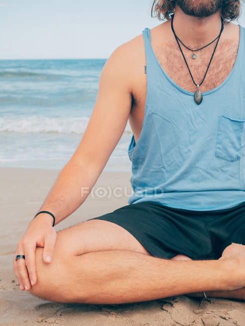 Обрізане зображення спортивного бородатого чоловіка, який тренується на спокійному узбережжі і робить йогу Асану проти блакитного моря і неба — стокове фото