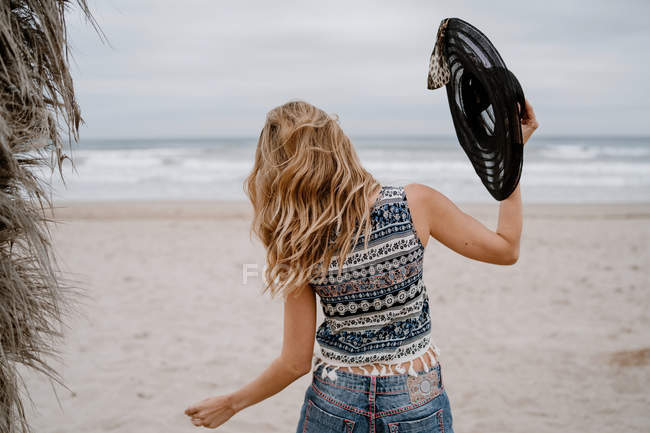 Belle femme portant un haut et un short dansant sur le bord de mer sablonneux avec un chapeau noir — Photo de stock