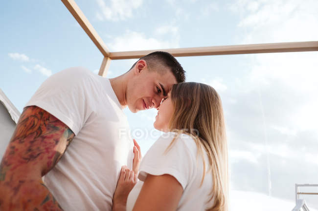 Vista lateral do jovem casal romântico em camisetas brancas e jeans ajoelhados e abraçando no quarto de glamping — Fotografia de Stock