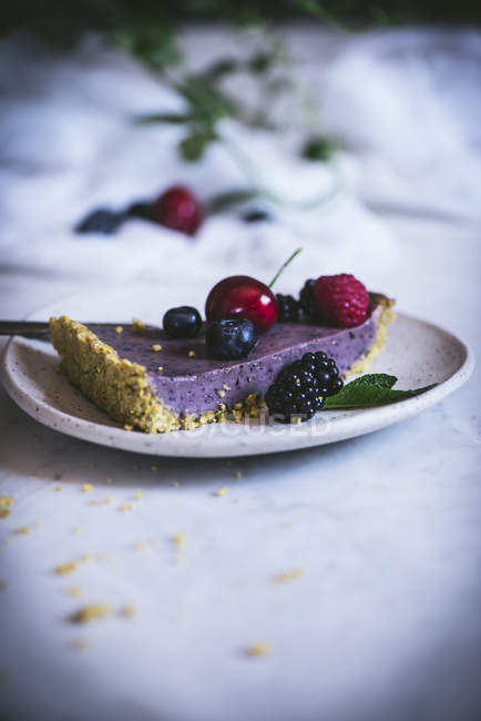 Morceau de gâteau savoureux avec des baies d'été sur assiette sur table blanche — Photo de stock