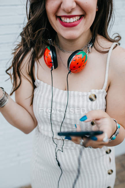 Обрезанное изображение молоденькой женщины, проверяющей плейлист в смартфоне на белом фоне, улыбающейся — стоковое фото