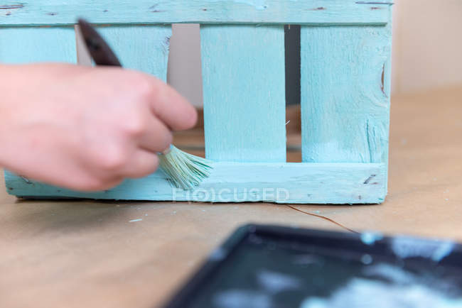 Крупный план женской руки, окрашивающей деревянную коробку в синий цвет кистью — стоковое фото